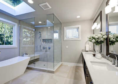 Spacious bathroom in gray tones with heated floors, freestanding tub, walk-in shower, double sink vanity and skylights.